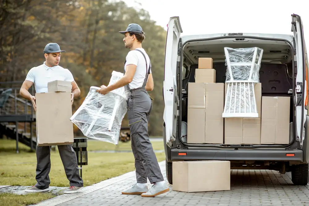 Twee verhuizers laden dozen en een stoel in een verhuisbus